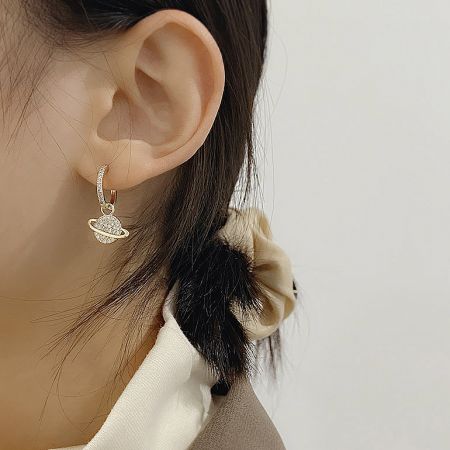 Macro shot of the gold Saturn charm, showing the detailed craftsmanship and embedded stones.