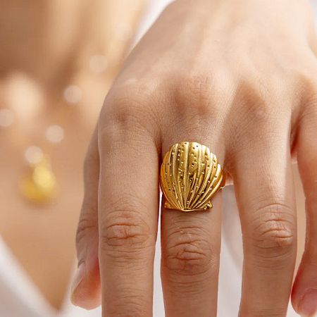 Close-up view of the gold seashell ring on a finger.