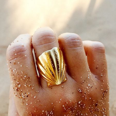 Stainless Steel Tarnish-Free Beach Jewelry Chunky Shell Open Rings Set of 5 - A model's hand wearing a gold-tone, chunky, shell-shaped open ring from the tarnish-free stainless steel beach jewelry set, resting on a sandy surface.