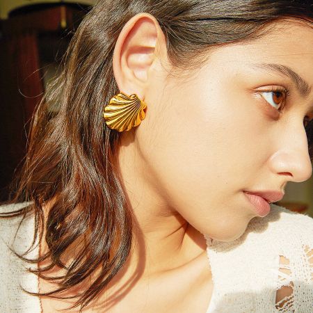 A model wearing the gold scallop shell earring, showcasing its size and how it looks when worn.