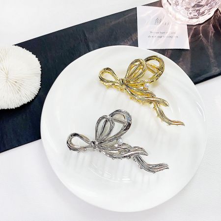 Metal Large Ribbon Hair Claw Clips with Pearl Accent - A pair of elegant metal bow-shaped hair claw clips, one in a polished gold finish and the other in a sleek silver finish, displayed on a white surface.