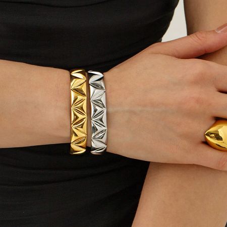 Gold and silver cuff bracelets from the set displayed with a matching ring.