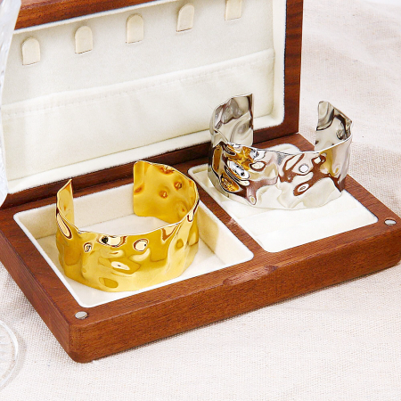 Gold and silver hammered cuff bracelets elegantly displayed in a wooden jewelry box.