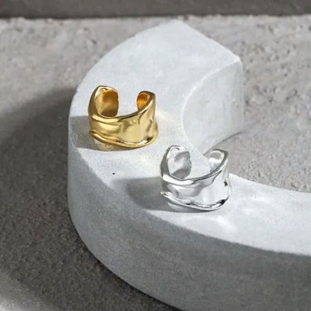 A set of gold and silver 925 sterling silver wide ear cuffs displayed on a stone platform, highlighting both available finishes.