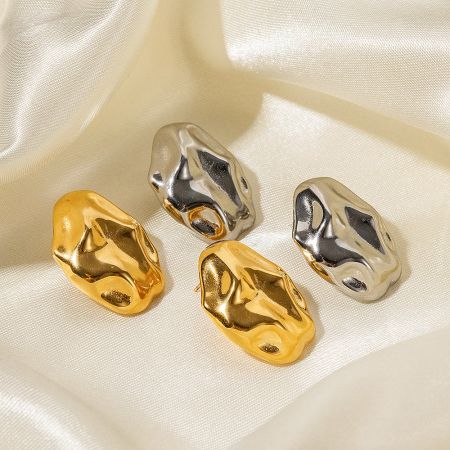 The gold and silver irregular stud earrings displayed on a luxurious satin fabric.