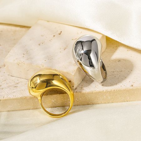Close-up of the gold and silver chunky rings on a neutral stone background.