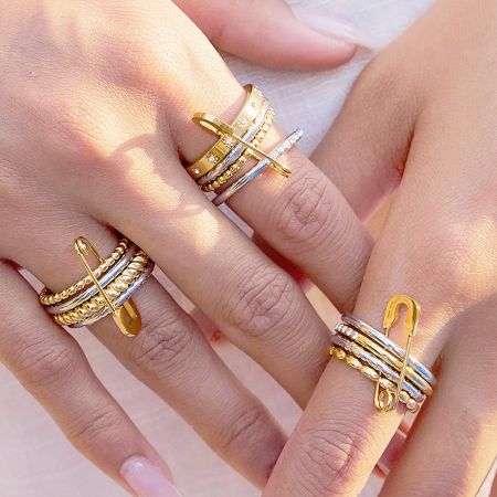 Model's hand showcasing the versatile styling of the mixed gold and silver stackable rings with the safety pin charm.