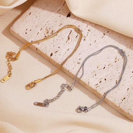 Detailed product shot of the gold and silver thin snake chain bracelets with the infinity knot symbol.