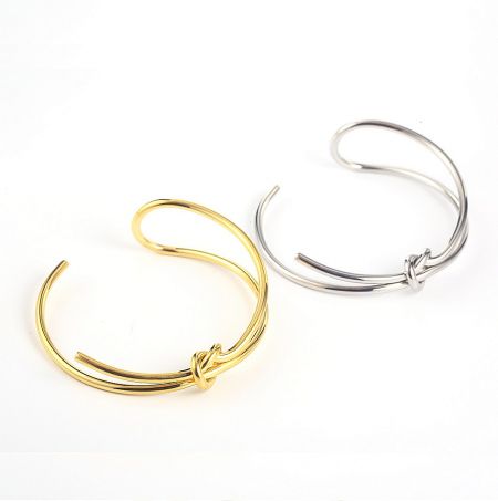 The Bow Cuff Bracelet shown in both gold and silver plating options, highlighting the twisted knot design.