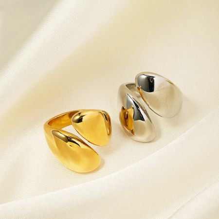 Close-up of two statement rings with a distinctive twisted design, one in gold and one in silver.
