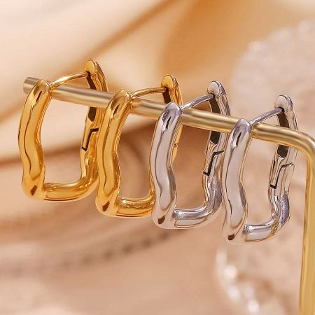 A pair of gold and silver plated stainless steel huggie hoop earrings displayed on a neutral background.