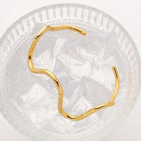 A creative shot of the gold wave cuff bangle in a glass bowl, emphasizing its cool and contemporary appeal.