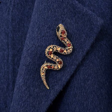 Close-up of a gold snake brooch with vibrant red and black gemstones on a dark blue fabric.