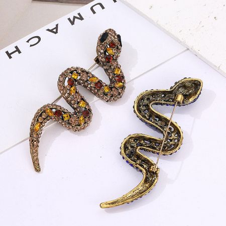Two detailed gold snake brooches, one with multi-colored gemstones and one with blue accents.