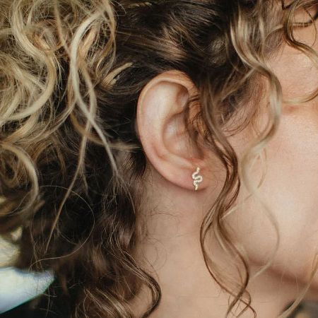 Close-up of a gold snake-shaped zircon stud earring worn on the ear.