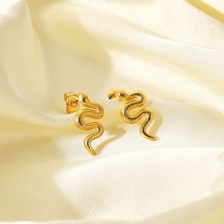 Close-up of gold snake earrings on a cream fabric background.