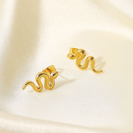 Detailed view of the gold snake earrings on a cream satin background.