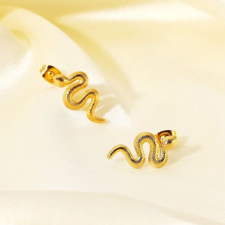 Another angle of the gold snake-shaped earrings on cream satin.