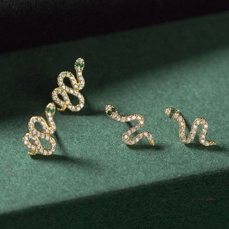 A luxurious pair of gold snake earrings featuring diamond-like scales and emerald-like eyes.