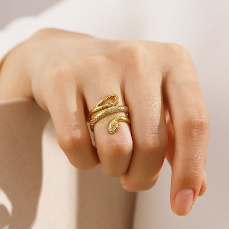 A close-up of the gold snake ring being worn on a finger, showcasing its detailed wrap design.
