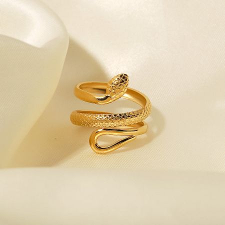 The gold snake ring with a textured surface resting on a luxurious cream-colored fabric.