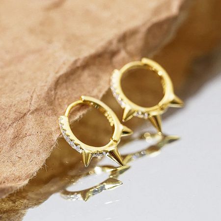 A pair of gold spiked earrings with diamond accents, highlighting the intricate details.