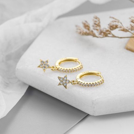 A pair of gold star charm huggie hoop earrings displayed on a neutral background.