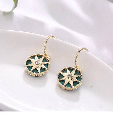 Detailed view of the gold star earring with a teal resin background and central gem.