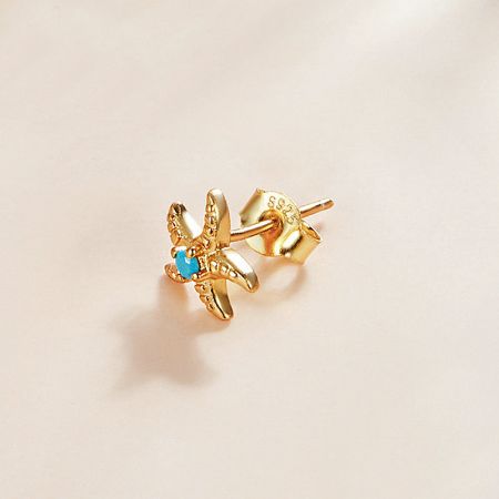 A pair of gold starfish earrings with central blue turquoise gemstones on a clean white background.