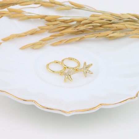 The gold starfish earrings with sparkling gemstones elegantly displayed on a decorative porcelain dish.