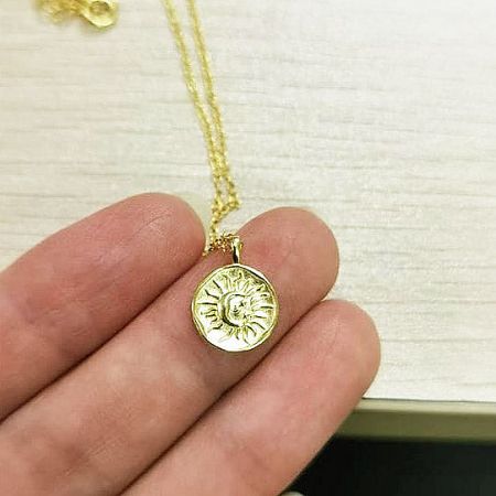 Detailed close-up of the gold sunburst coin pendant on the sterling silver necklace.