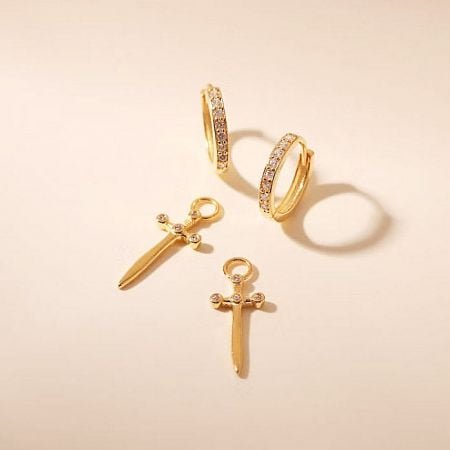 A set of three gold jewelry pieces including two sword earrings and a zirconia hoop.