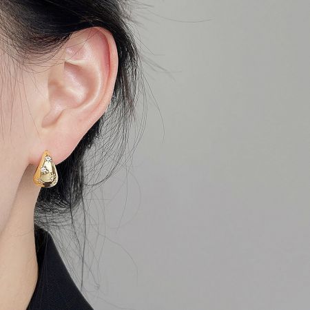 A model wearing one of the gold teardrop-shaped earrings from the set, showing how it looks when worn.