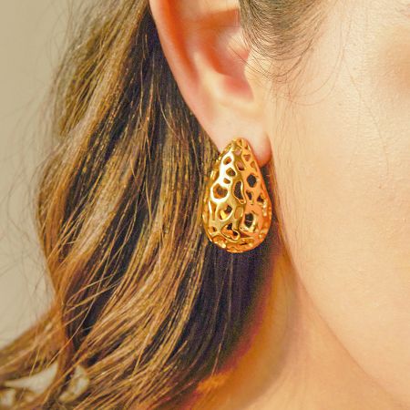 A close-up view of the gold teardrop earring being worn, highlighting its textured design.