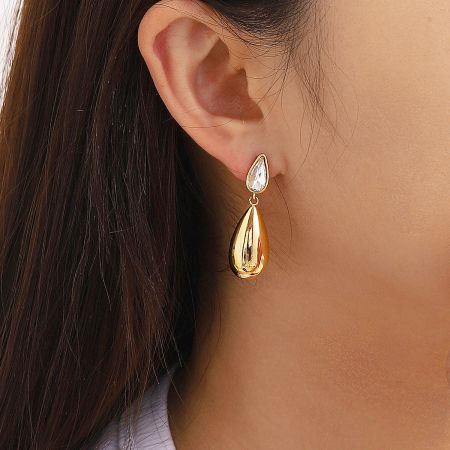 Close-up of a single gold teardrop earring highlighting the clear crystal detail.
