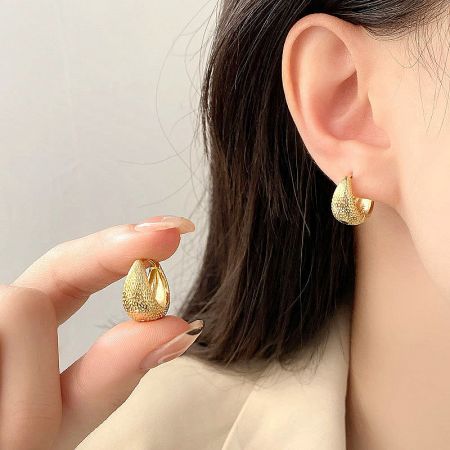 A close-up of the gold textured bag-shape hoop earring, showing its unique teardrop form and detailed surface.