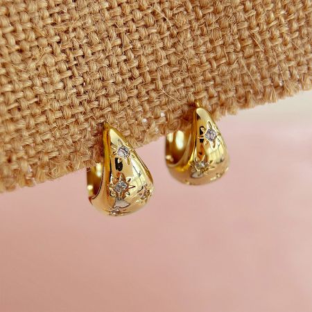A pair of gold teardrop earrings from the set, featuring intricate diamond starburst embellishments.