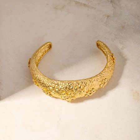 Detailed view of the intricate hammered texture and floral design on the gold cuff bangle.