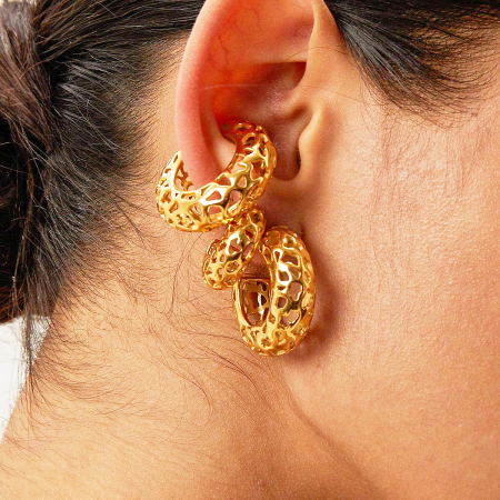 Close-up shot of the gold-plated C-shaped earring on a model's ear, showing its scale and texture.