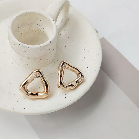 The gold-plated geometric triangle hoop earrings elegantly displayed on a textured ceramic plate.