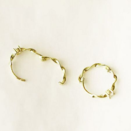 Close-up of a shiny gold twist hoop earring, showcasing the detailed rope-like design.