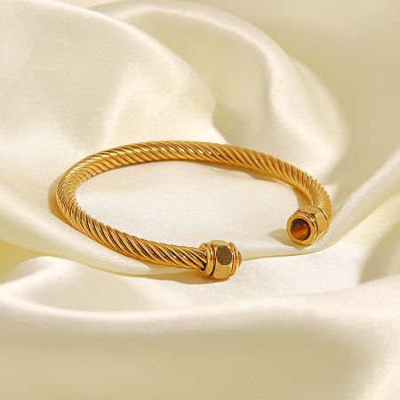 A single gold-plated twisted bangle with elegant stone accents, shown on a neutral background.
