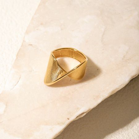 Product shot of a twisted gold-colored stainless steel ring on a stone.