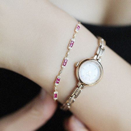 The sterling silver ruby bracelet displayed alongside a classic gold watch, illustrating a perfect pairing.