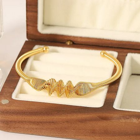 A single gold wave-patterned bangle elegantly presented in a wooden jewelry box.