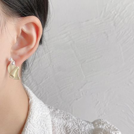 Side view of a woman wearing a gold wavy earring with two pearls.