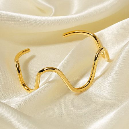 Close-up of the 18K gold plated curve wave cuff bangle on a luxurious cream satin background.
