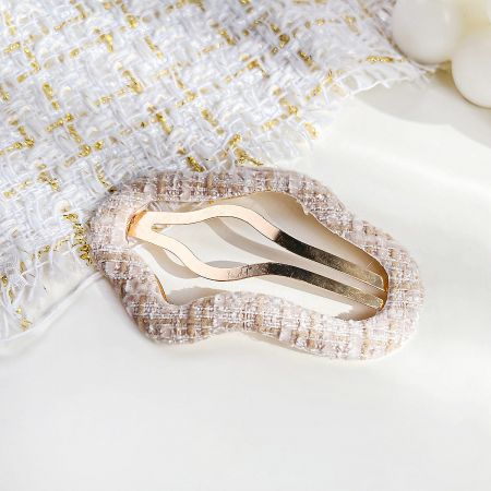 A close-up of a gold wavy hair clip on a decorative fabric background.
