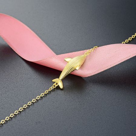 Matching gold whale pendant necklace on a dark background.