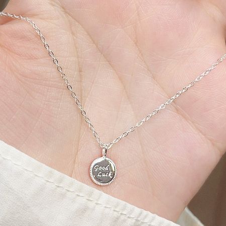The 'Good Luck' silver necklace held in a hand to show its scale and delicate nature.